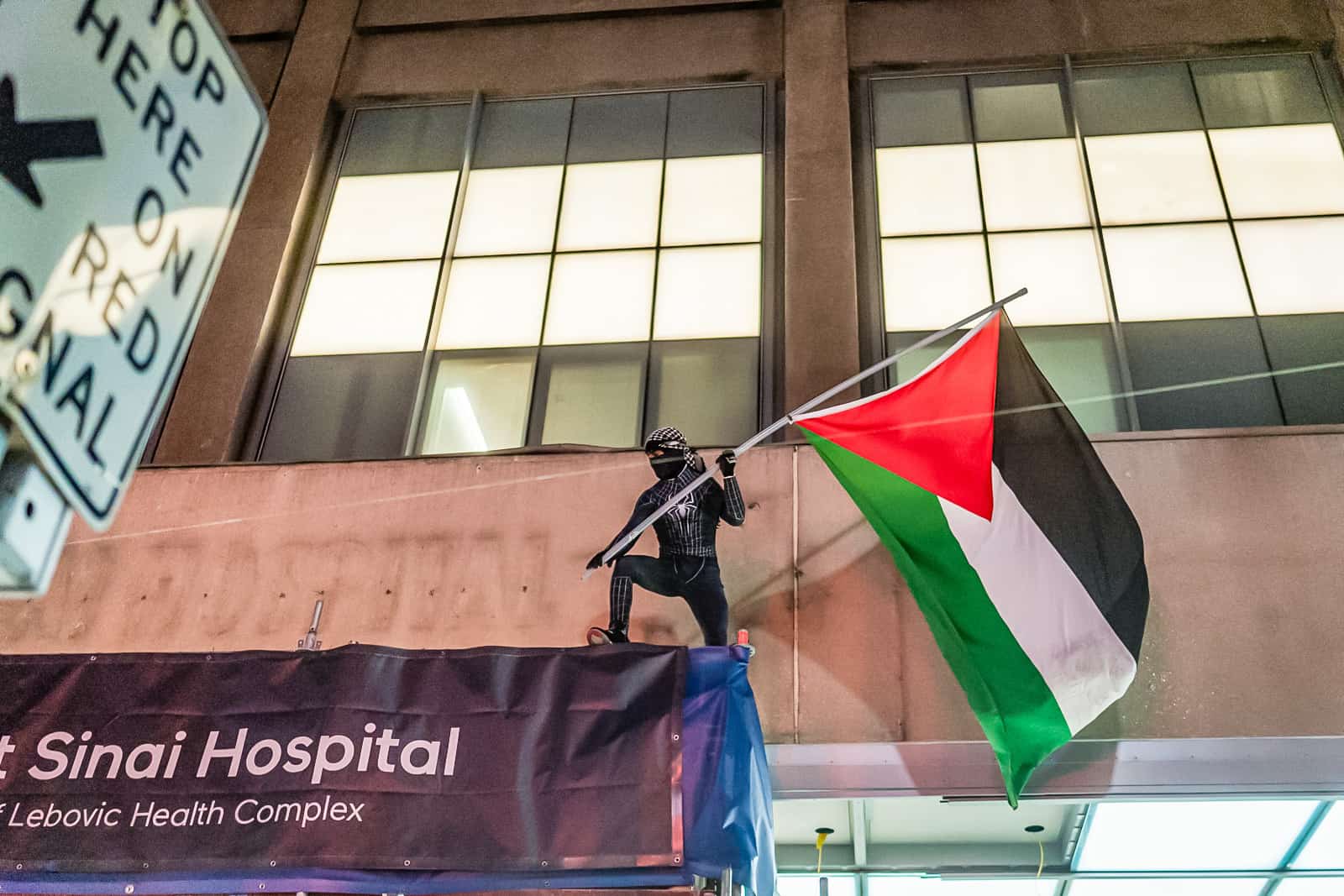 A demonstrator dressed as Spiderman costume waves a Palestinian flag above the entrance of Mount Sinai Hospital as the rally goes by. Photo: Joshua Best